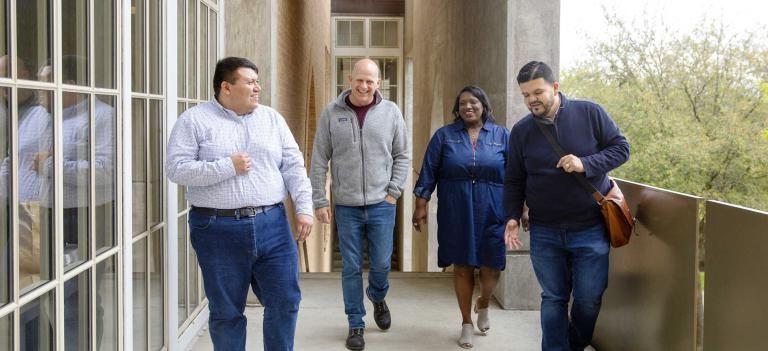 Four graduate students walk, talk and laugh together as they approach the entrance of The Bill Munday School of Business.