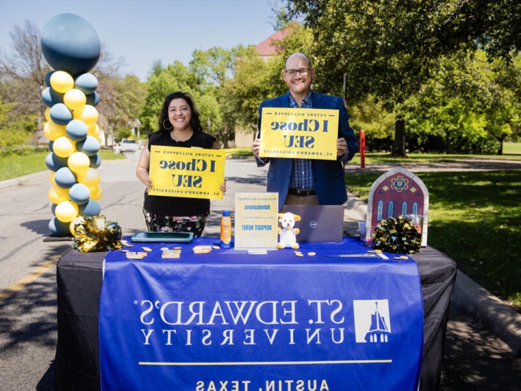 Two admission counselors stand at a table with A St. 365比分网电竞 banner on it and hold I Chose SEU signs.