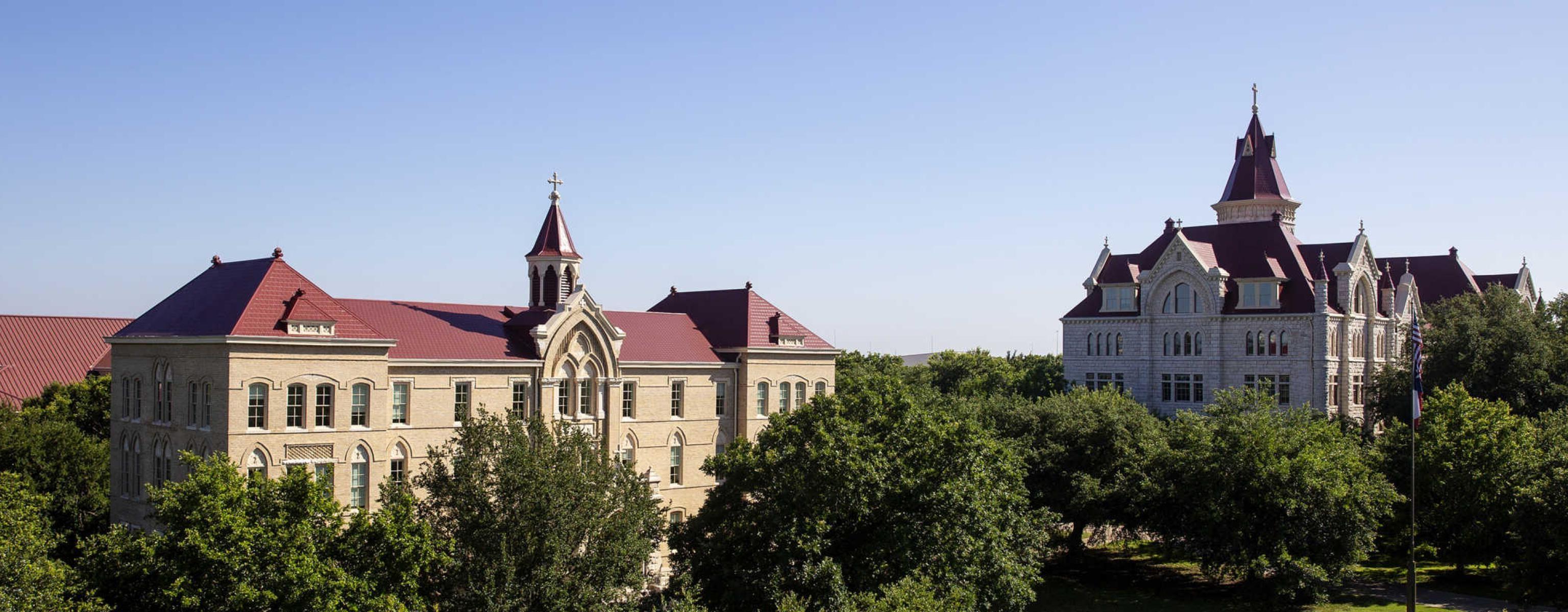 An aerial view of Main Building and Holy Cross Hall, surrounded by lush trees and green grass.